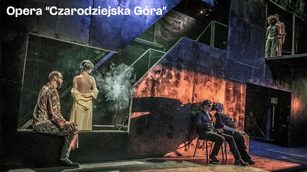 Stage scene from opera 'Czarodziejska Góra' with actors in dramatic poses and moody lighting.